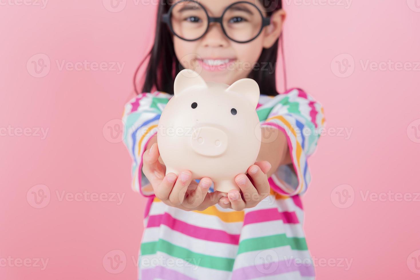 Little Asian girl saving money in a piggy bank, learning about saving, Kid save money for future education. Money, finances, insurance, and people concept photo