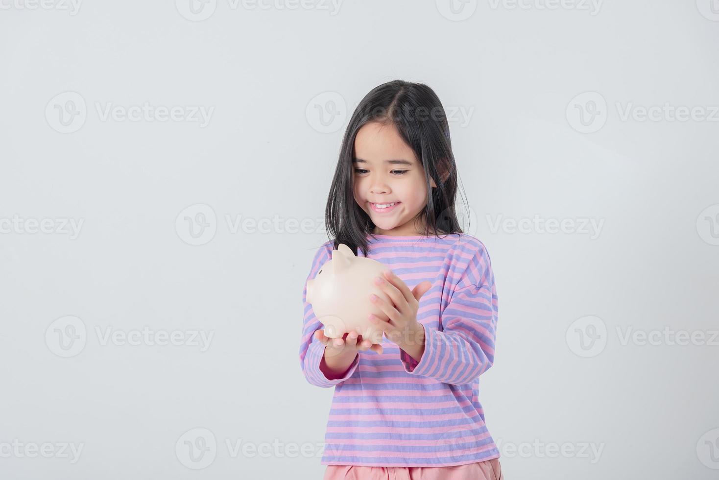 Little Asian girl saving money in a piggy bank, learning about saving, Kid save money for future education. Money, finances, insurance, and people concept photo