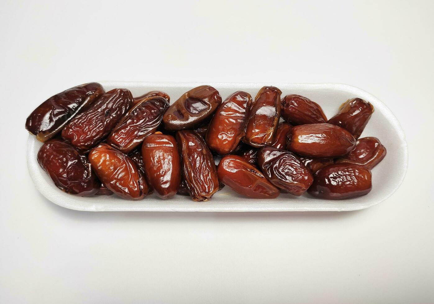 pile of dates fruit in white styrofoam tray, white background photo
