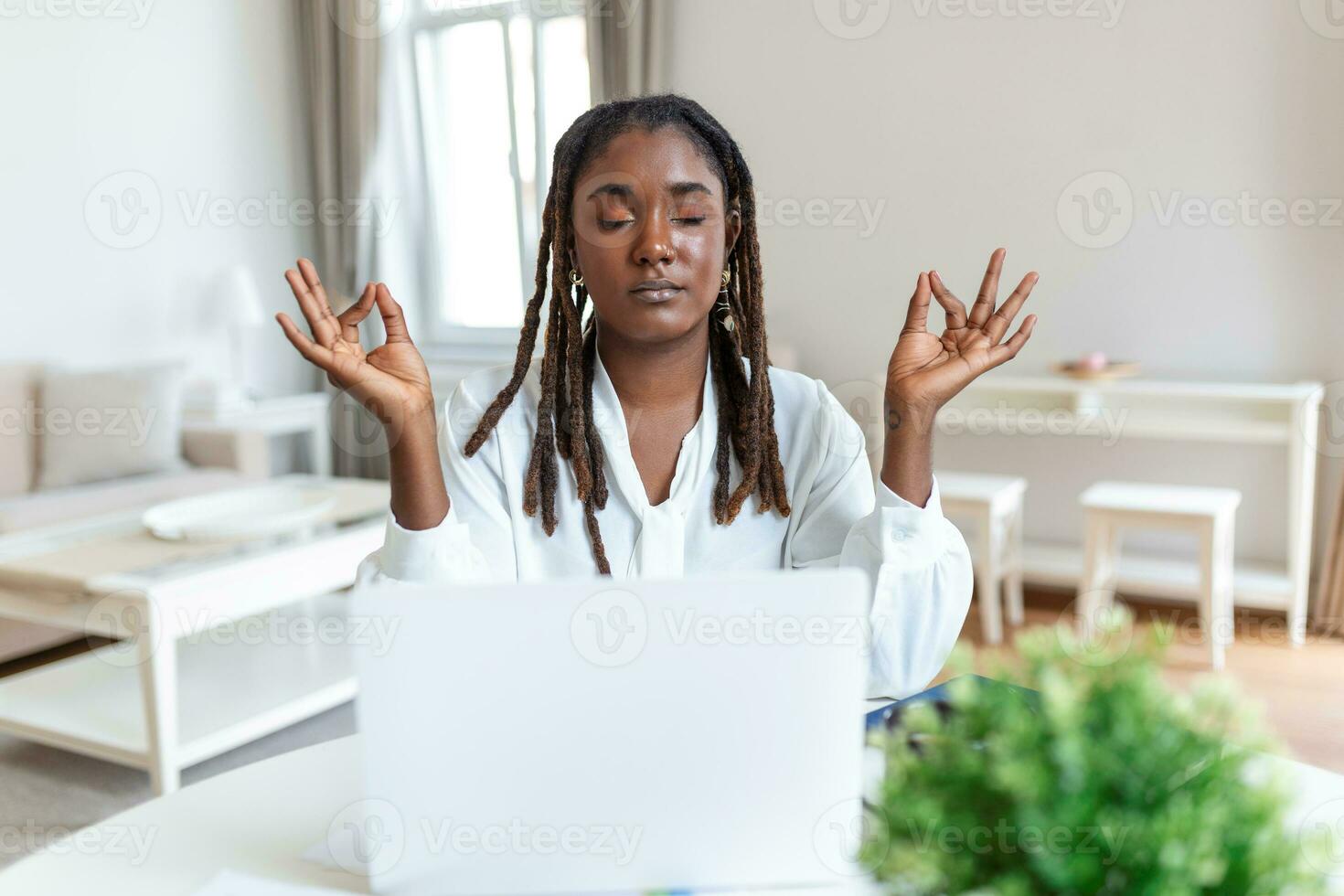Calm African female executive meditating taking break at work for mental balance, mindful businesswoman feeling relief and no stress doing yoga at work ignoring avoiding stressful job photo