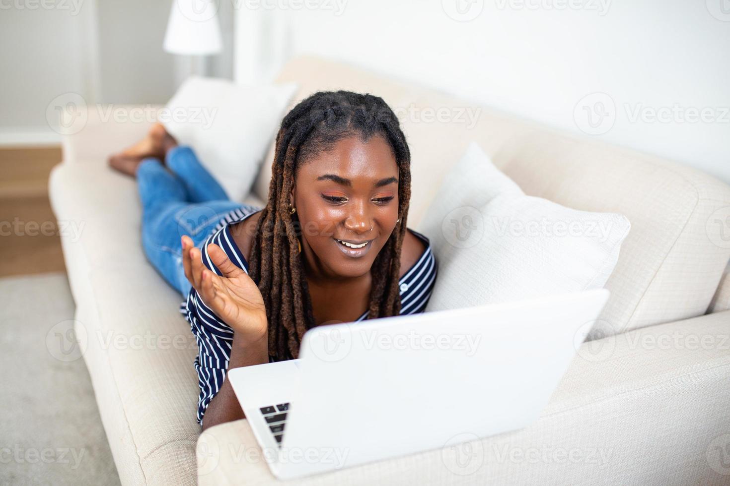Beautiful African woman freelancer noting information for planning project doing remote job via laptop computer. Girl laughing while reading email on modern laptop device . photo