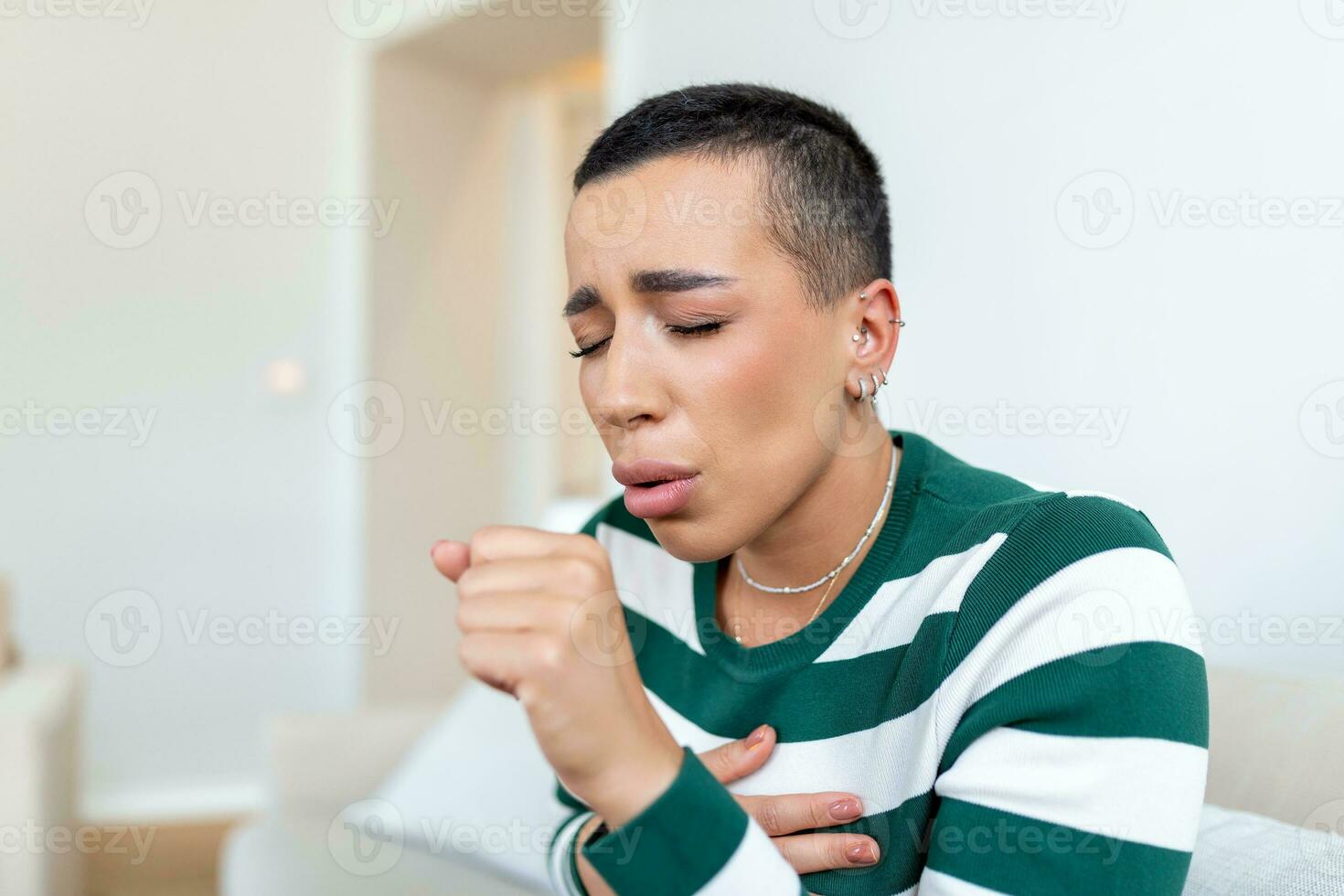 Portrait of Sick Young African American Woman Coughing. Sick young woman sitting on sofa and having cough while suffering from sore throat photo