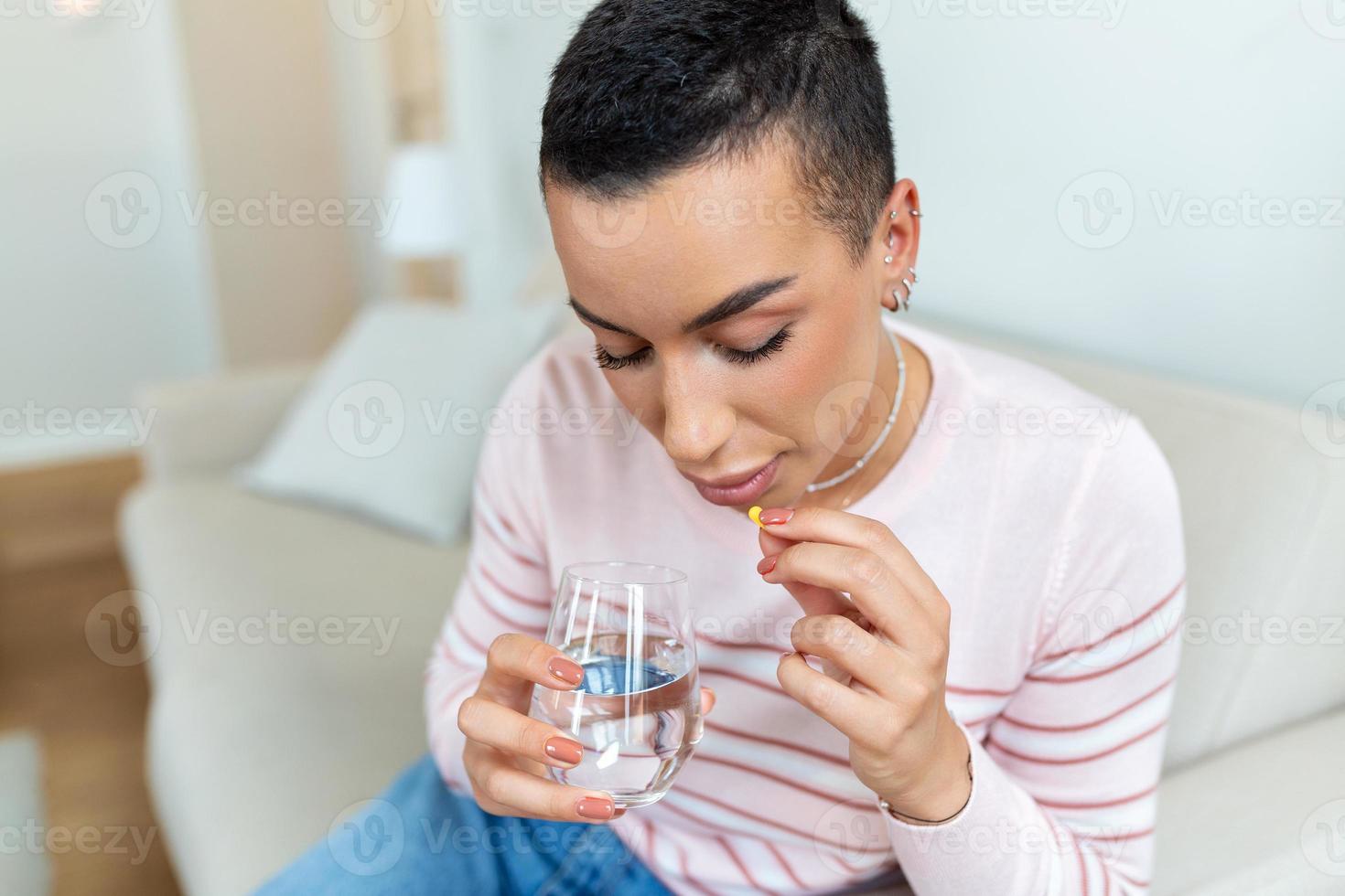 Millennial ill sick woman taking painkiller medicine to relieve stomachache pain sit on bed in the morning. Sick woman lying in bed with high fever. Cold flu and migraine. photo