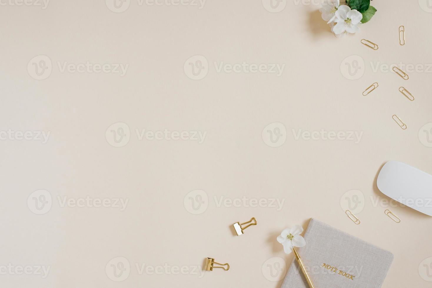Top view of a table with a notebook and pen, mouse, paper clips and clips, white apple blossom on a beige table. Flat lay, copy space photo