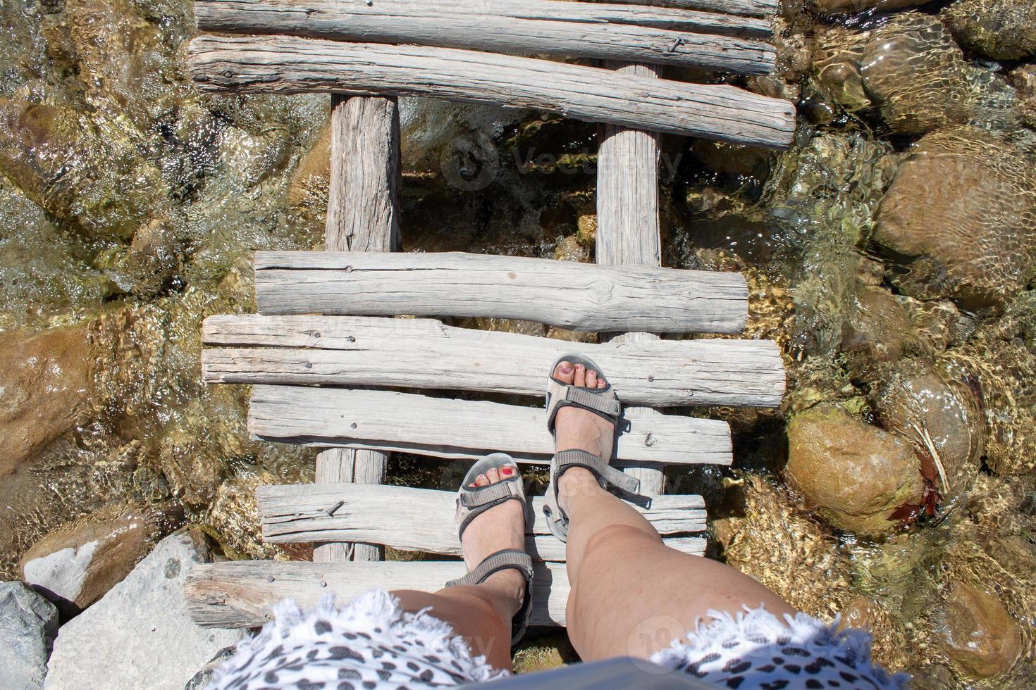 Woman's legs on an old wooden bridge through the river photo