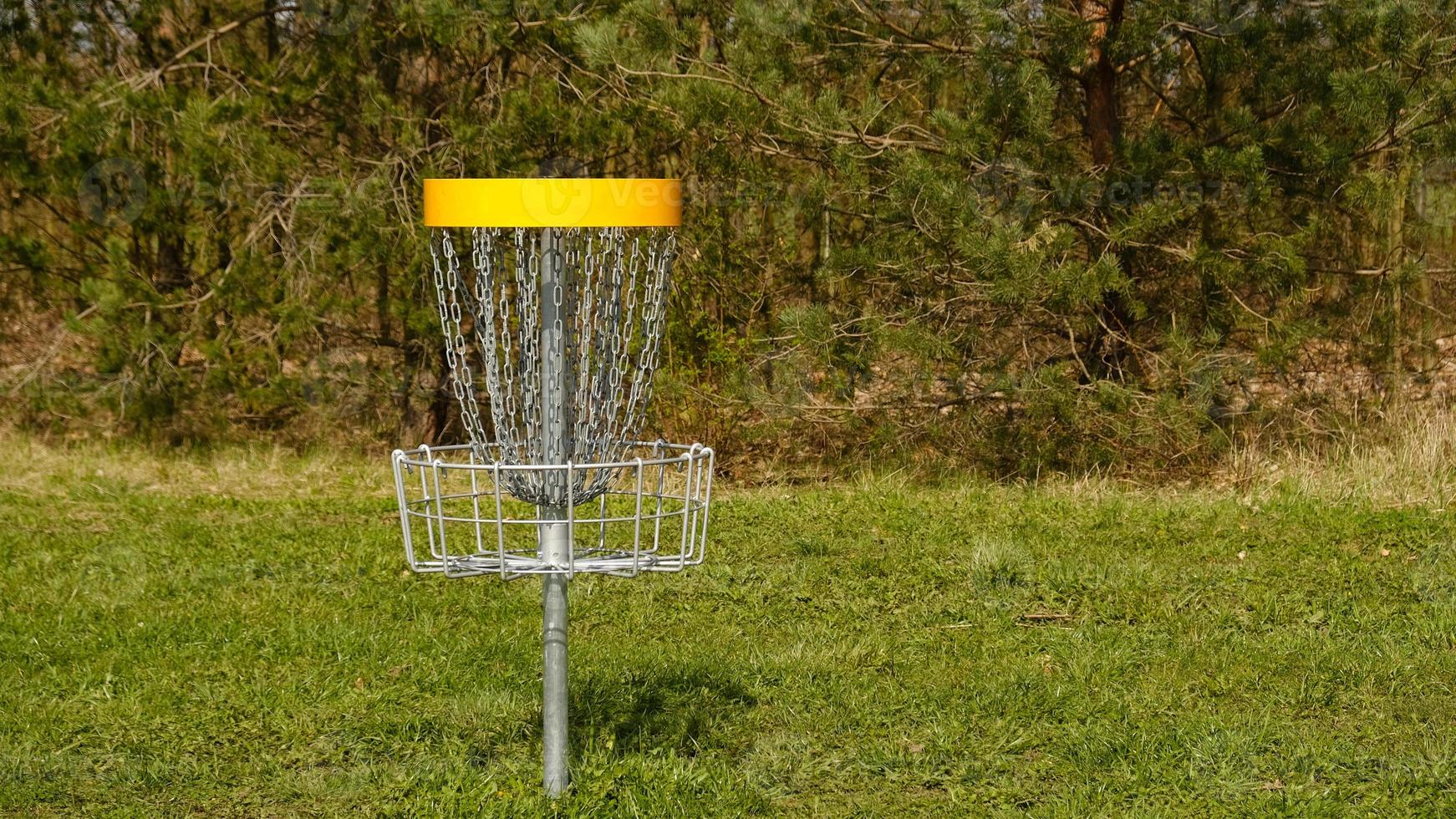 Disc Golf basket. Frisbee golf is sport and hobbie in outdoor park. Metal basket with chains for disc game surrounded by vibrant green trees. photo