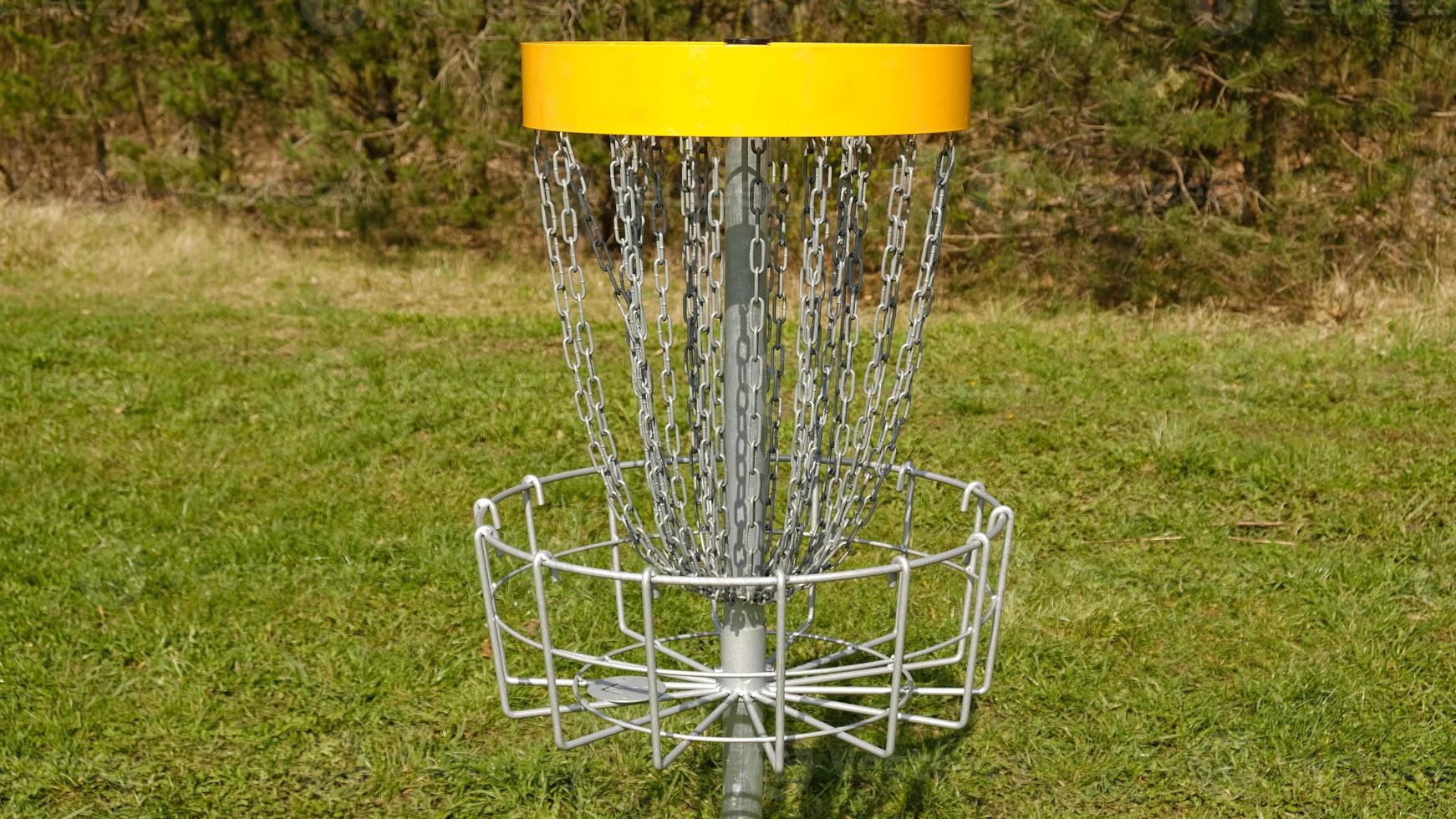 Disc Golf basket. Frisbee golf is sport and hobbie in outdoor park. Metal basket with chains for disc game surrounded by vibrant green trees. photo