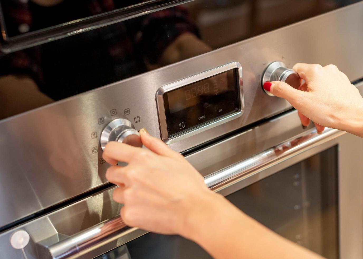 de cerca hembra mano apertura o clausura moderno eléctrico horno preparar a cocinar en el moderno cocina. foto