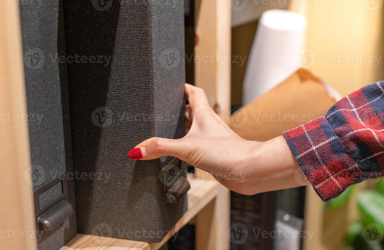 Female hand picking new dark grey file binder on shelf in stationary shop. photo