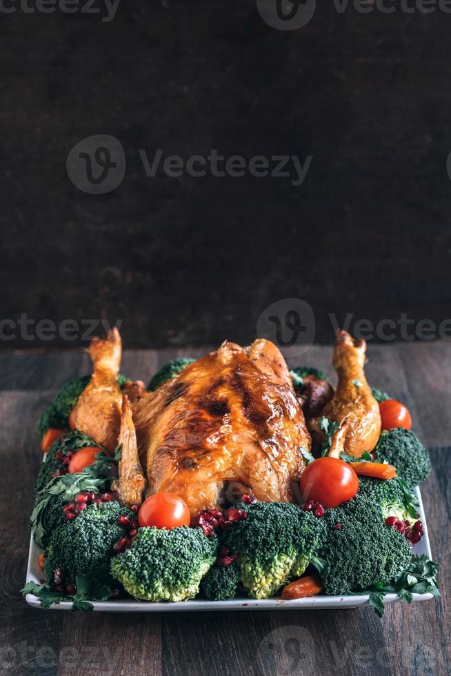 Roasted chicken with vegetables on wooden table photo