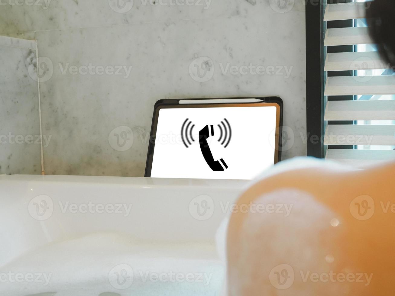 Young woman soaking in bathtub with incoming call photo