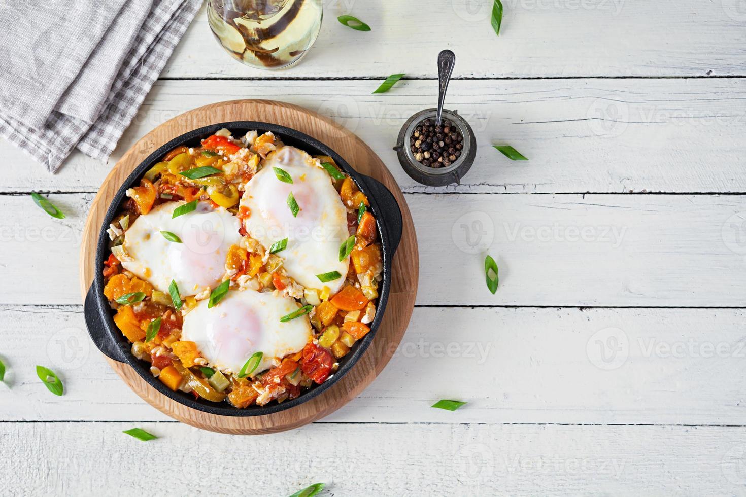 Shakshouka in frying pan. Fried eggs with vegetables, tomato, pepper, pumpkin and onion. Top view photo