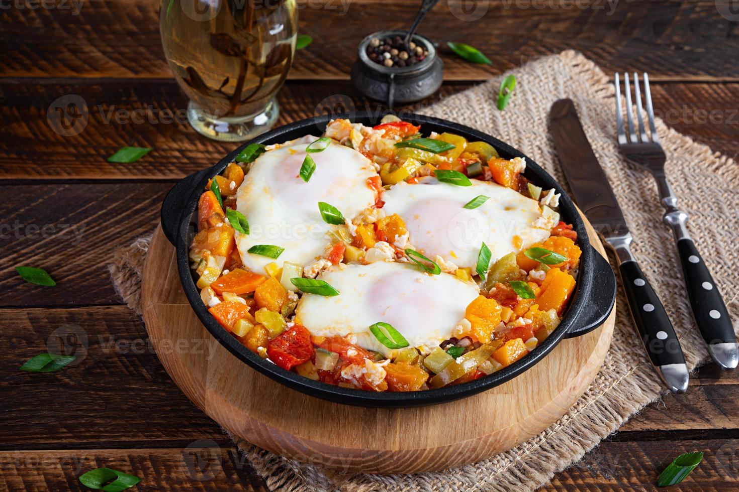 Shakshouka in frying pan. Fried eggs with vegetables, tomato, pepper, pumpkin and onion photo