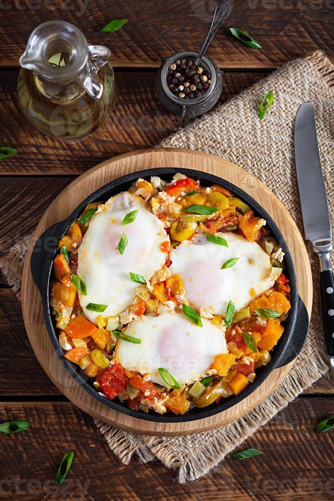 Shakshouka in frying pan. Fried eggs with vegetables, tomato, pepper, pumpkin and onion. Top view photo