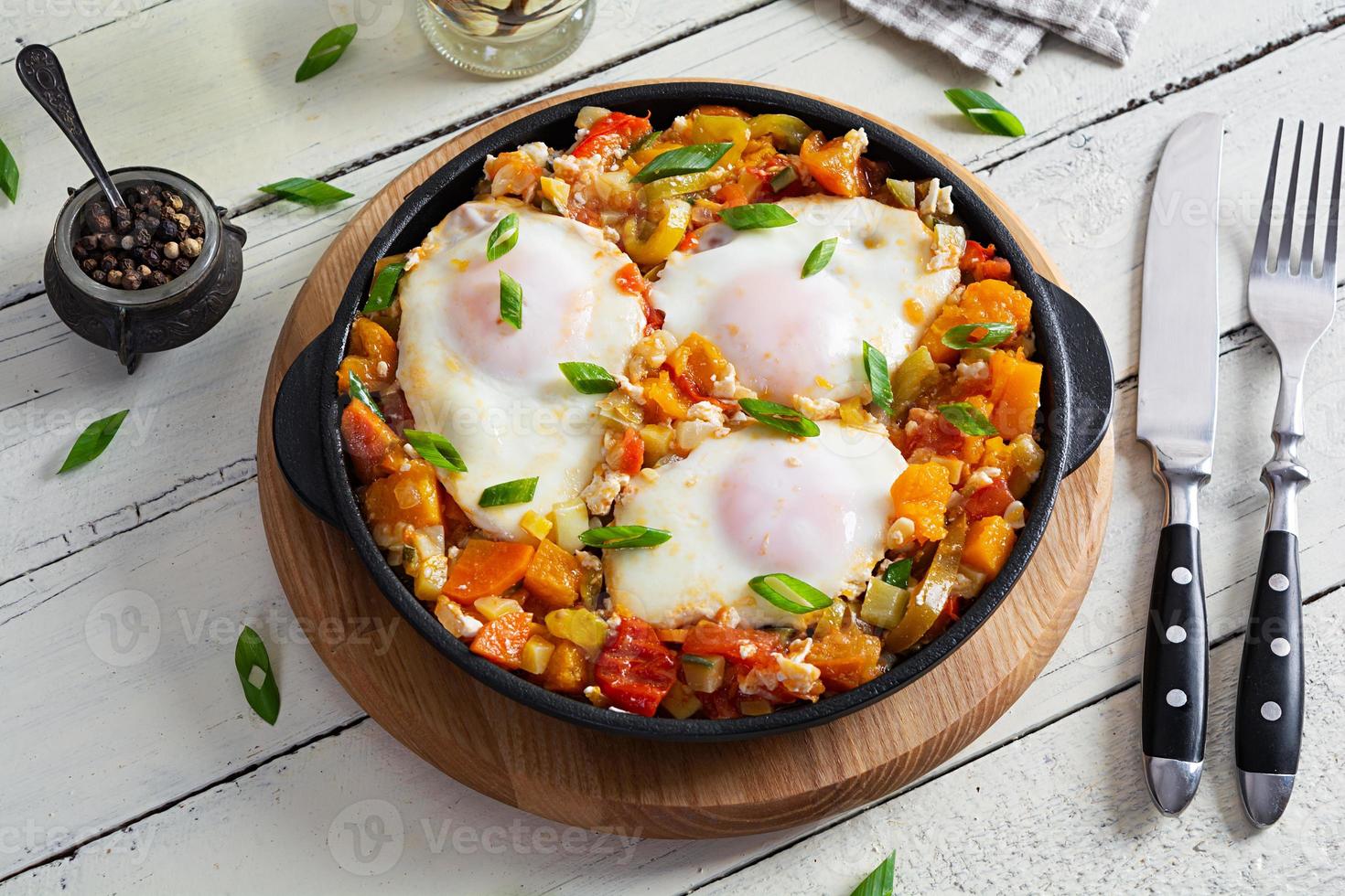 Shakshouka in frying pan. Fried eggs with vegetables, tomato, pepper, pumpkin and onion photo