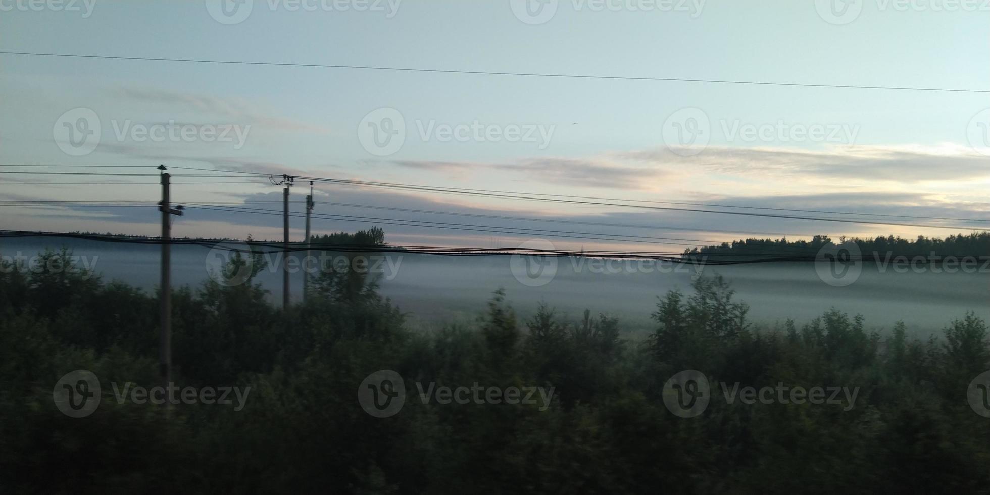 View from a moving train. Mist over the forest. Sunset sky. photo