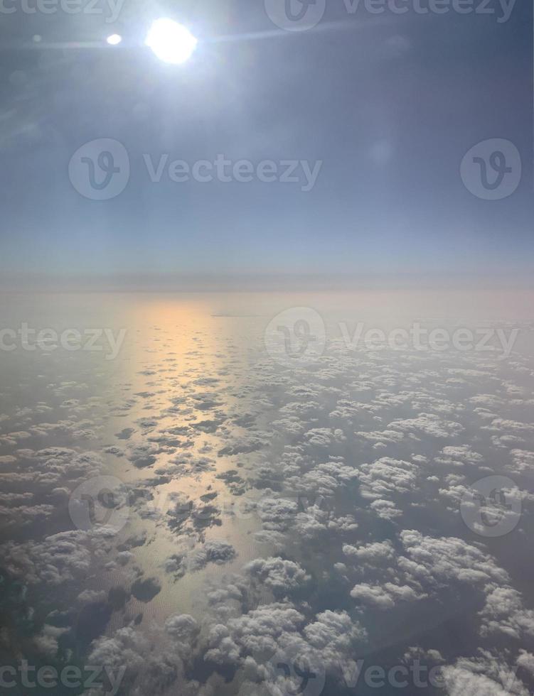 Sky travel. View from the illuminator. Fluffy white clouds. Sunlight pink and yellow reflexion on the water. Blue sky background. photo