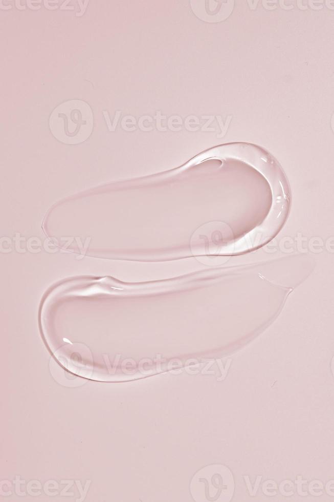 Squeezed cosmetic clear cream gel texture Iisolated on beige background. Close up transparent serum drop smears photo