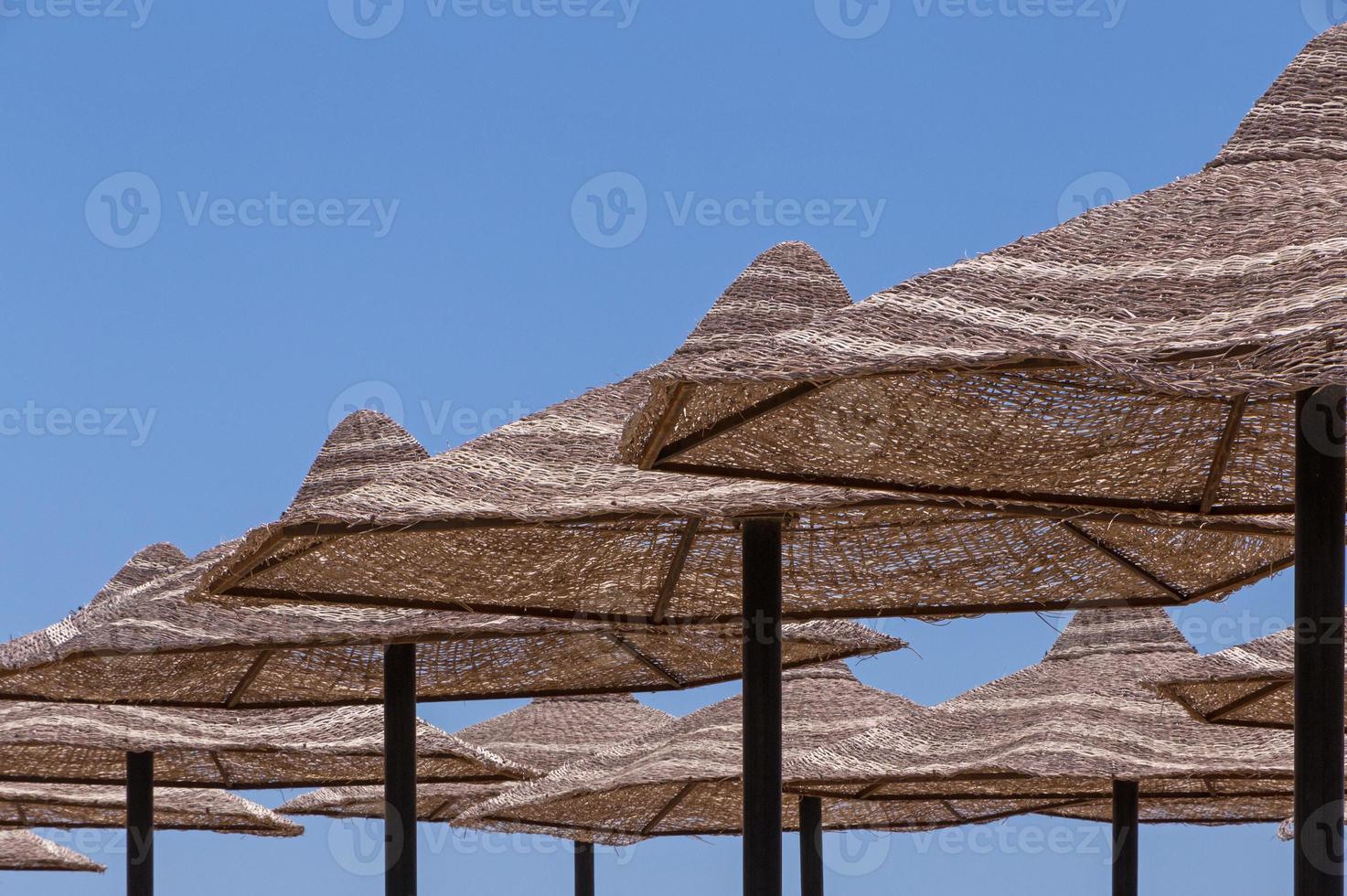 rows of sunshade straw beach umbrellas against blue sky photo