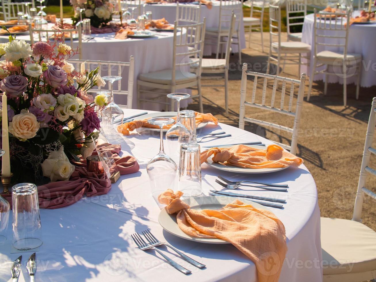 Wedding banquet concept. Chairs and round table for guests, served with cutler and, flowers and crockery and covered with a tablecloth photo