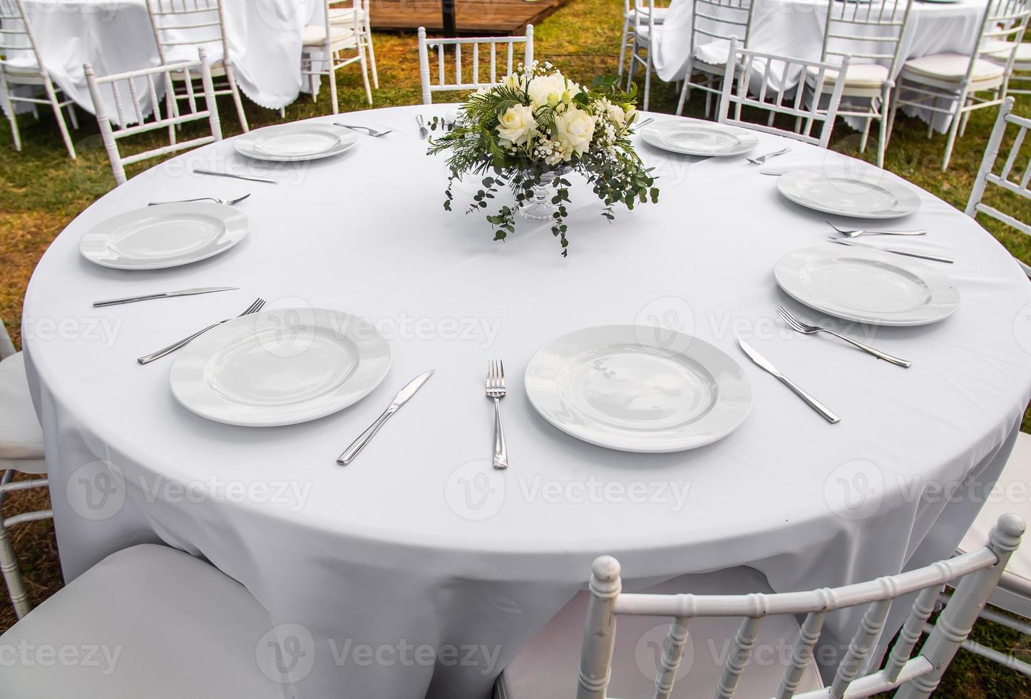 Beautiful outdoor wedding decoration in city. Candles and dried flowers and accessories with bouquets and glasses on table with linen tablecloth on newlywed table on green lawn photo