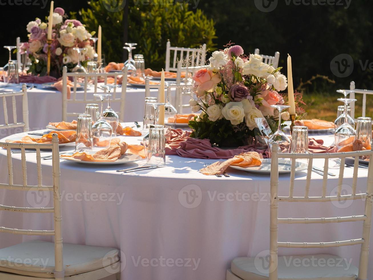Beautiful outdoor wedding decoration in city. Candles and dried flowers and accessories with bouquets and glasses on table with linen tablecloth on newlywed table on green lawn photo