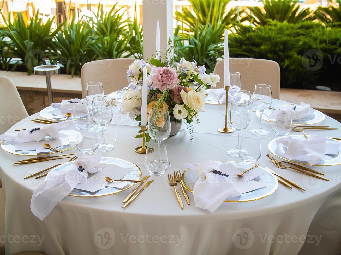 Wedding banquet concept. Chairs and round table for guests, served with cutler and, flowers and crockery and covered with a tablecloth photo