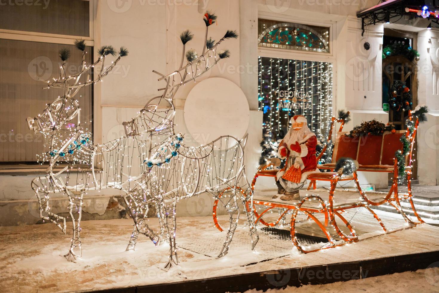 LEDs figure Santa Claus riding on sleigh during Christmas against restaurant or store in holiday winter city - festive and holidays season photo