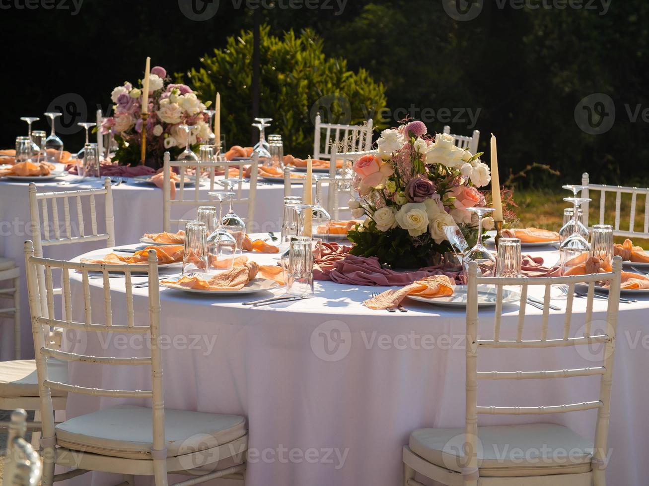 Wedding banquet concept. Chairs and round table for guests, served with cutler and, flowers and crockery and covered with a tablecloth photo