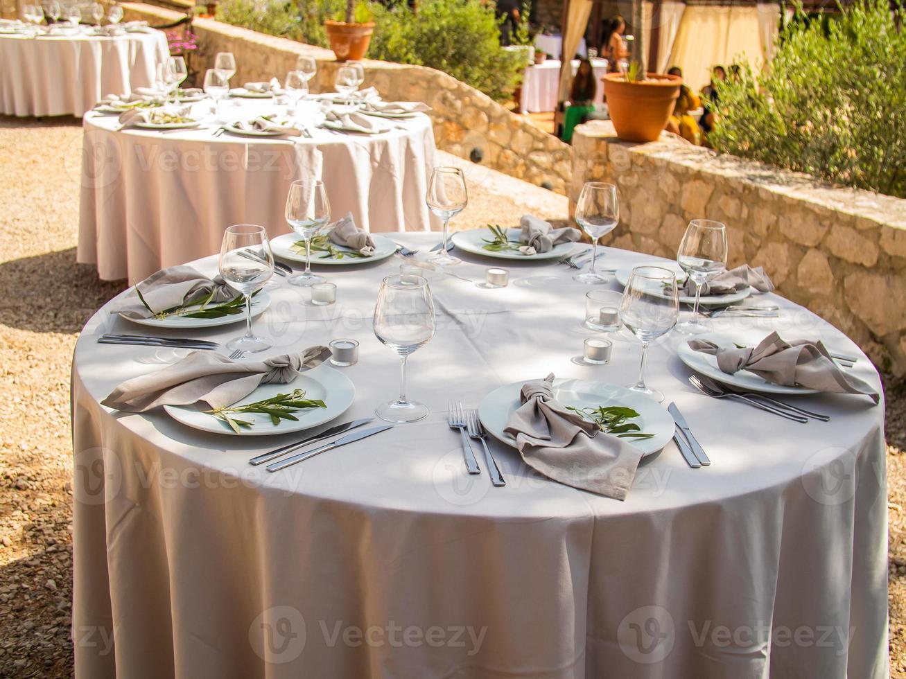Beautiful outdoor wedding decoration in city. Candles and dried flowers and accessories with bouquets and glasses on table with linen tablecloth on newlywed table on green lawn photo