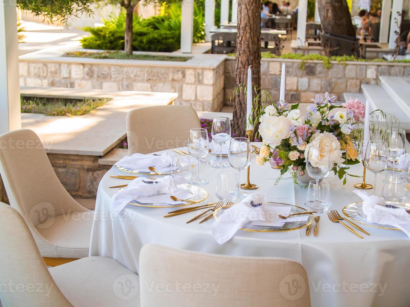 Wedding banquet concept. Chairs and round table for guests, served with cutler and, flowers and crockery and covered with a tablecloth photo