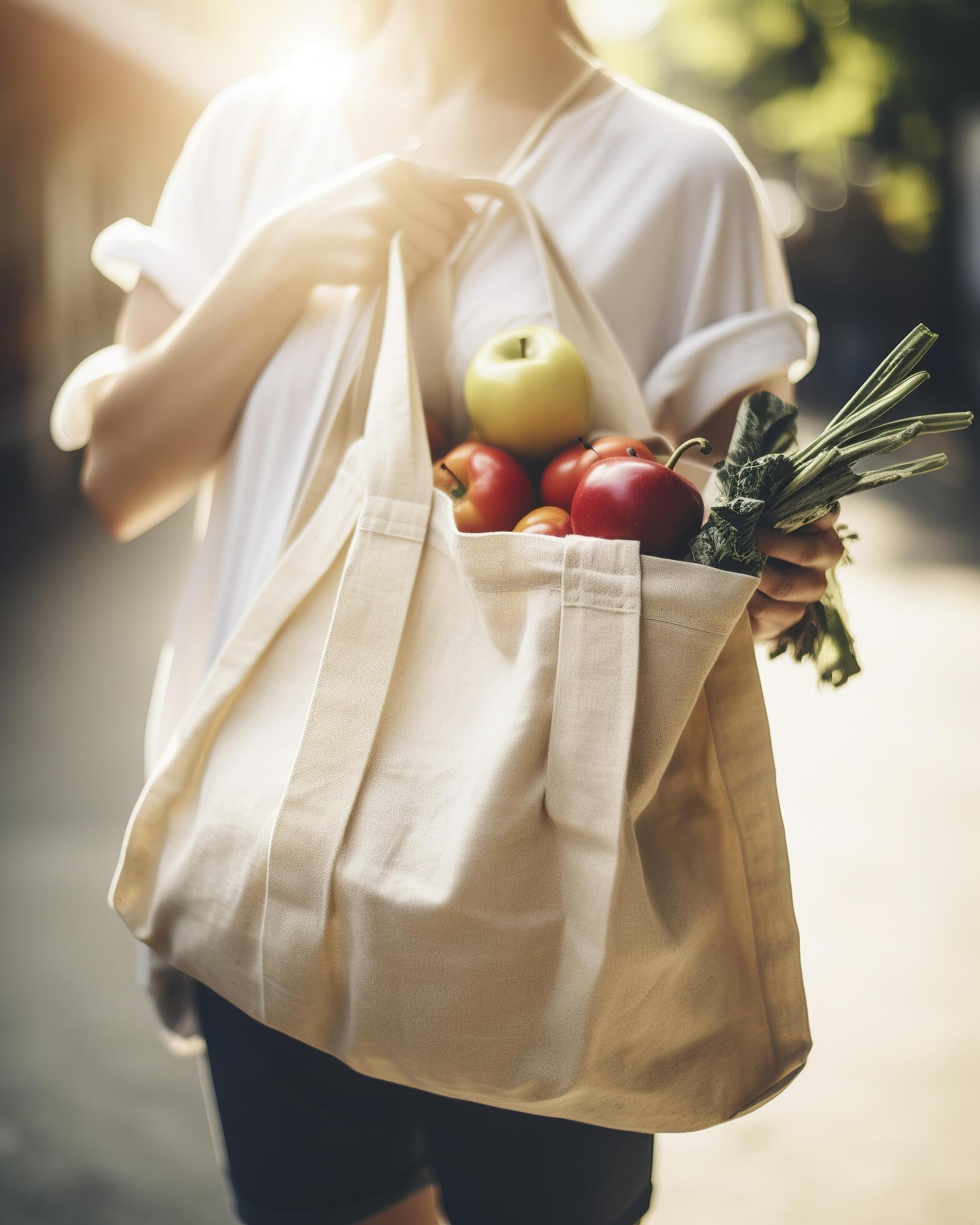 A woman carrying a reusable grocery bag full of fresh fruits and