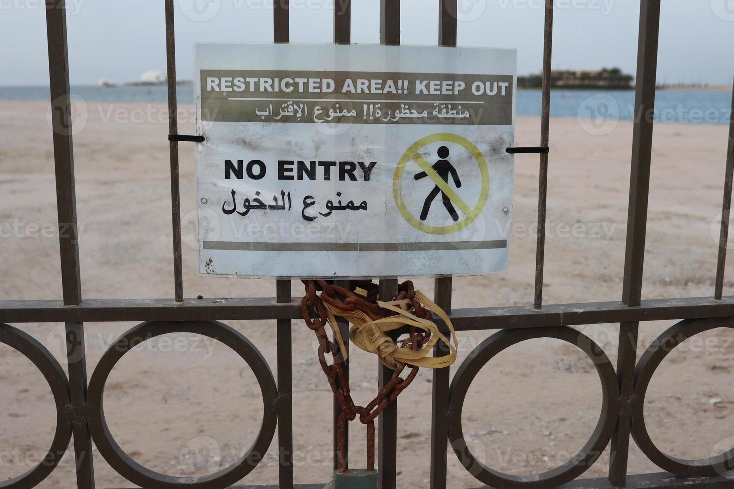 English Arabic sign located entrance,No entery sign board on metal gate with chain and lock photo