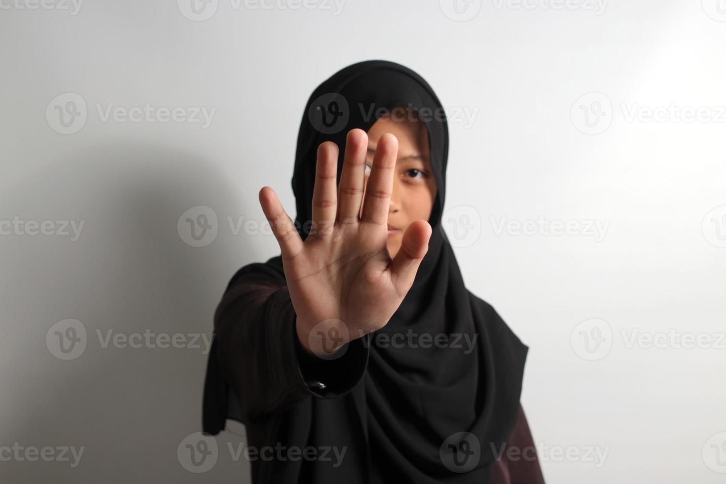 Displeased young Asian girl in hijab making stop gesture isolated on white background. photo