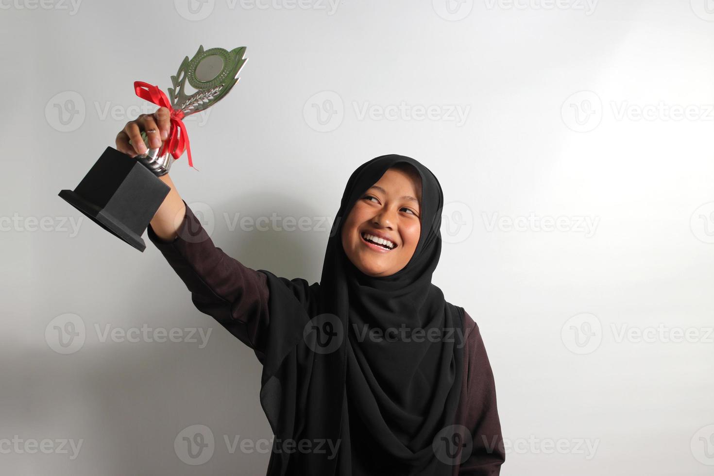Clever young Asian girl student in hijab raising her trophy isolated on white background. photo