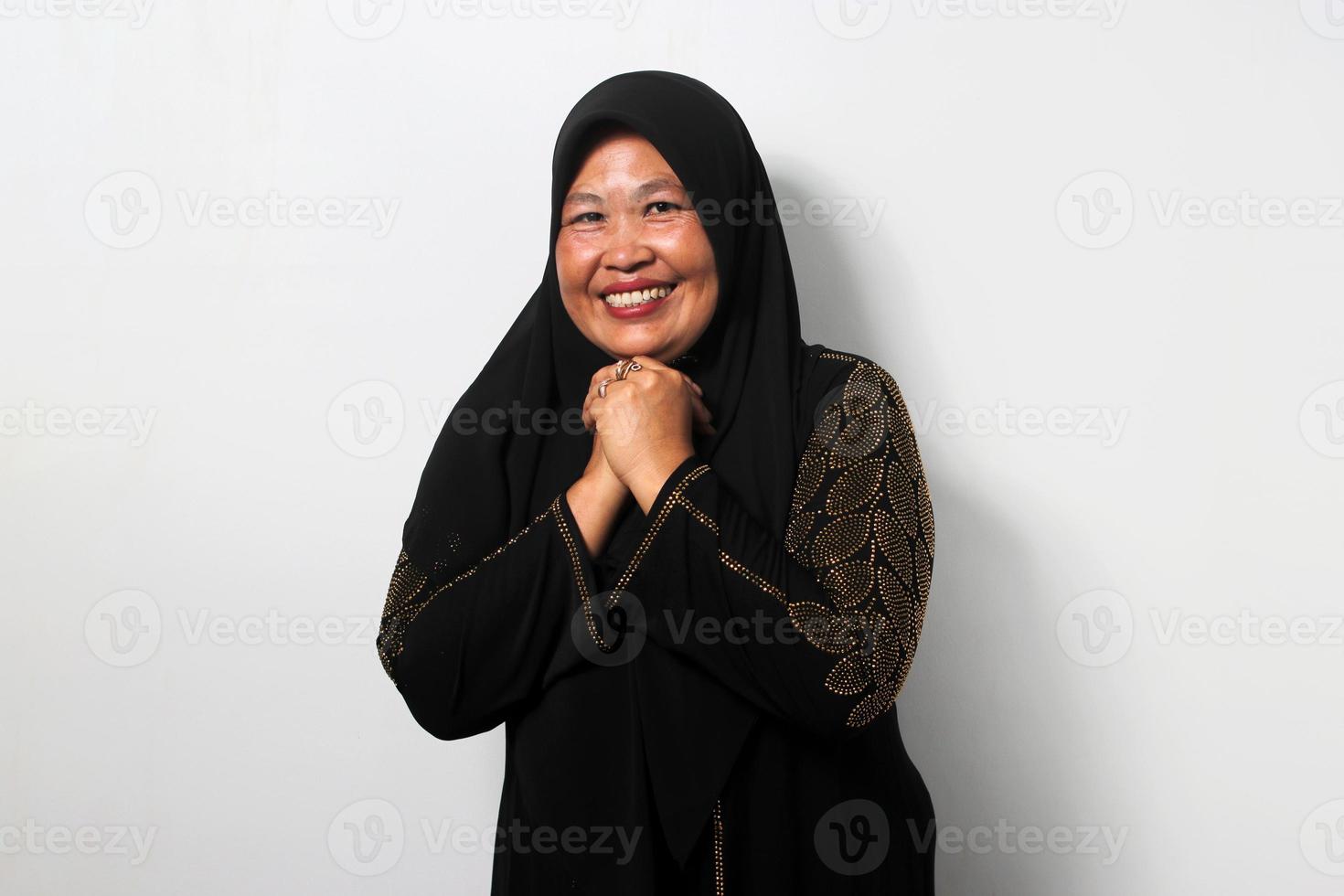 Excited Middle aged Asian women wearing hijab clenched her fist on her chin hoping for something photo