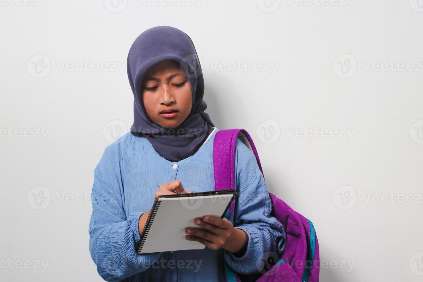 Young Asian girl student in hijab writing something on the book isolated on white background. photo