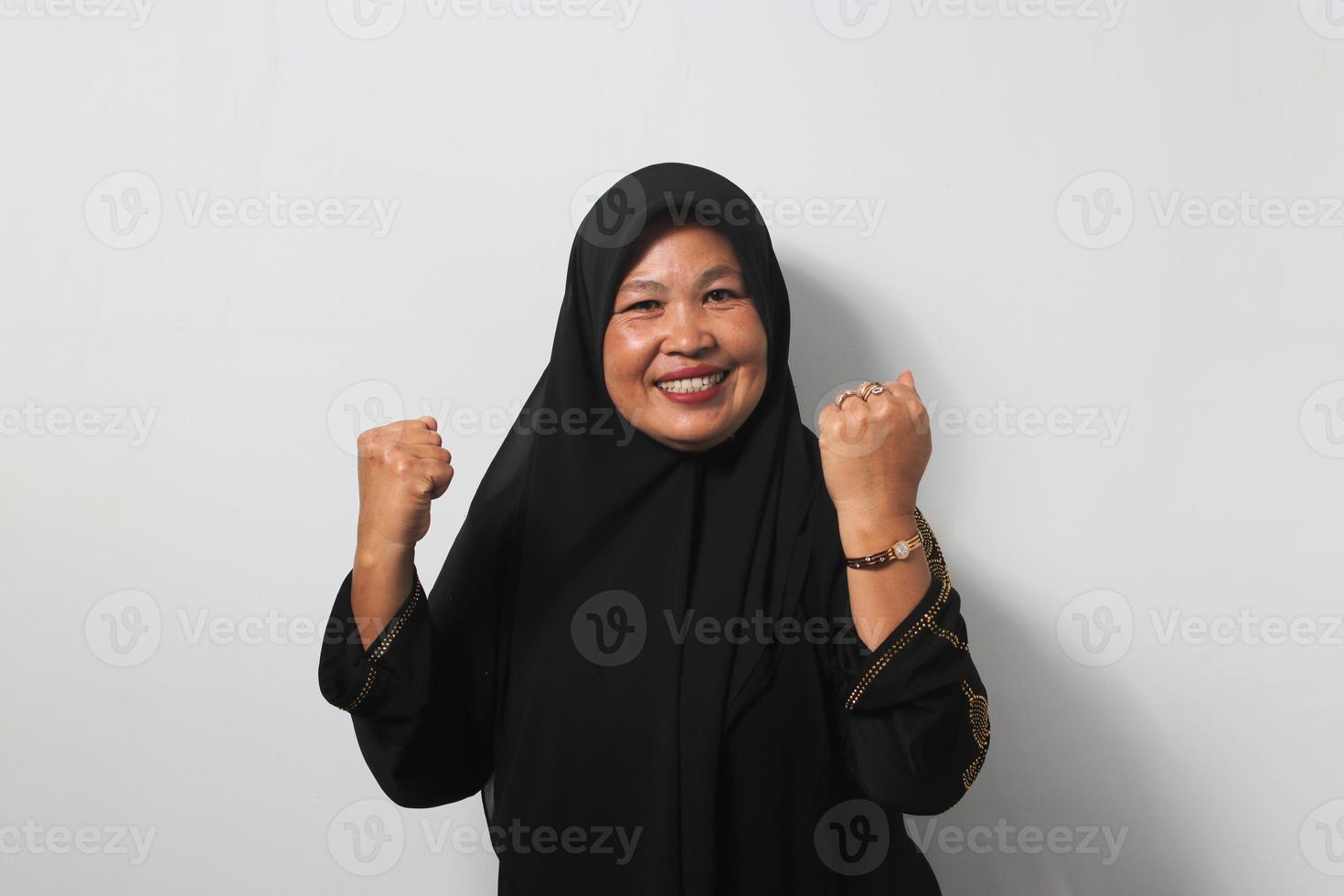 Strong Middle aged Asian women wearing hijab raises arms and looking at camera photo