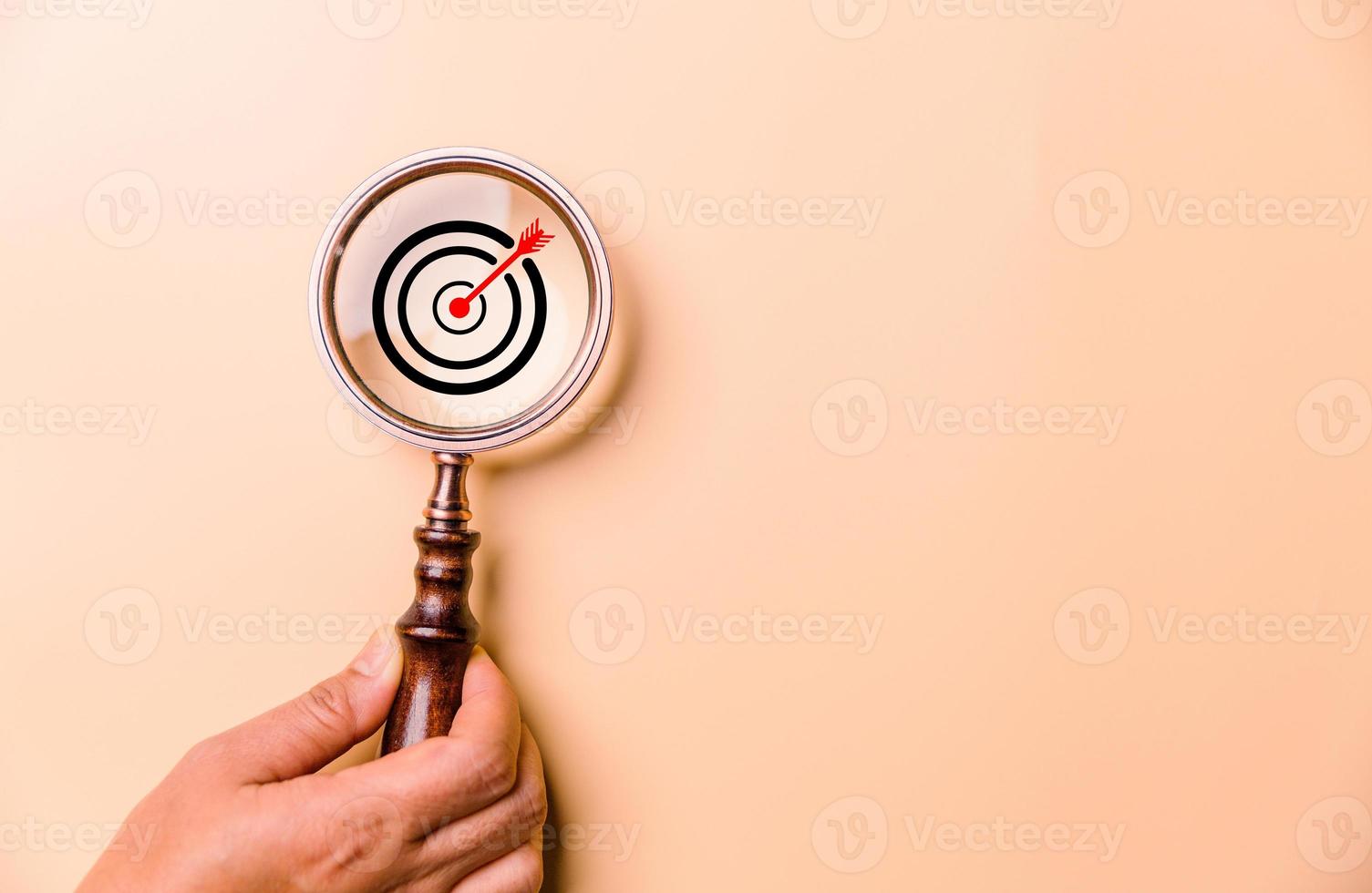 Hand holding target board inside vintage magnifying glass for focus business objective on orange background and copy space. Search, goal, strategy, success. successful marketing strategy goals photo