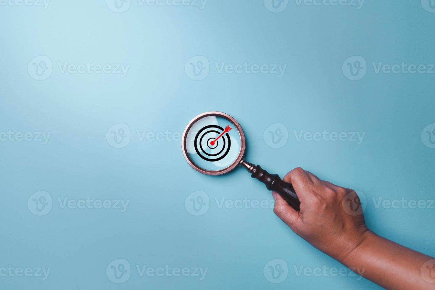 Hand holding target board inside vintage magnifying glass for focus business objective on blue background and copy space. Search, goal, strategy, success. successful marketing strategy goals photo