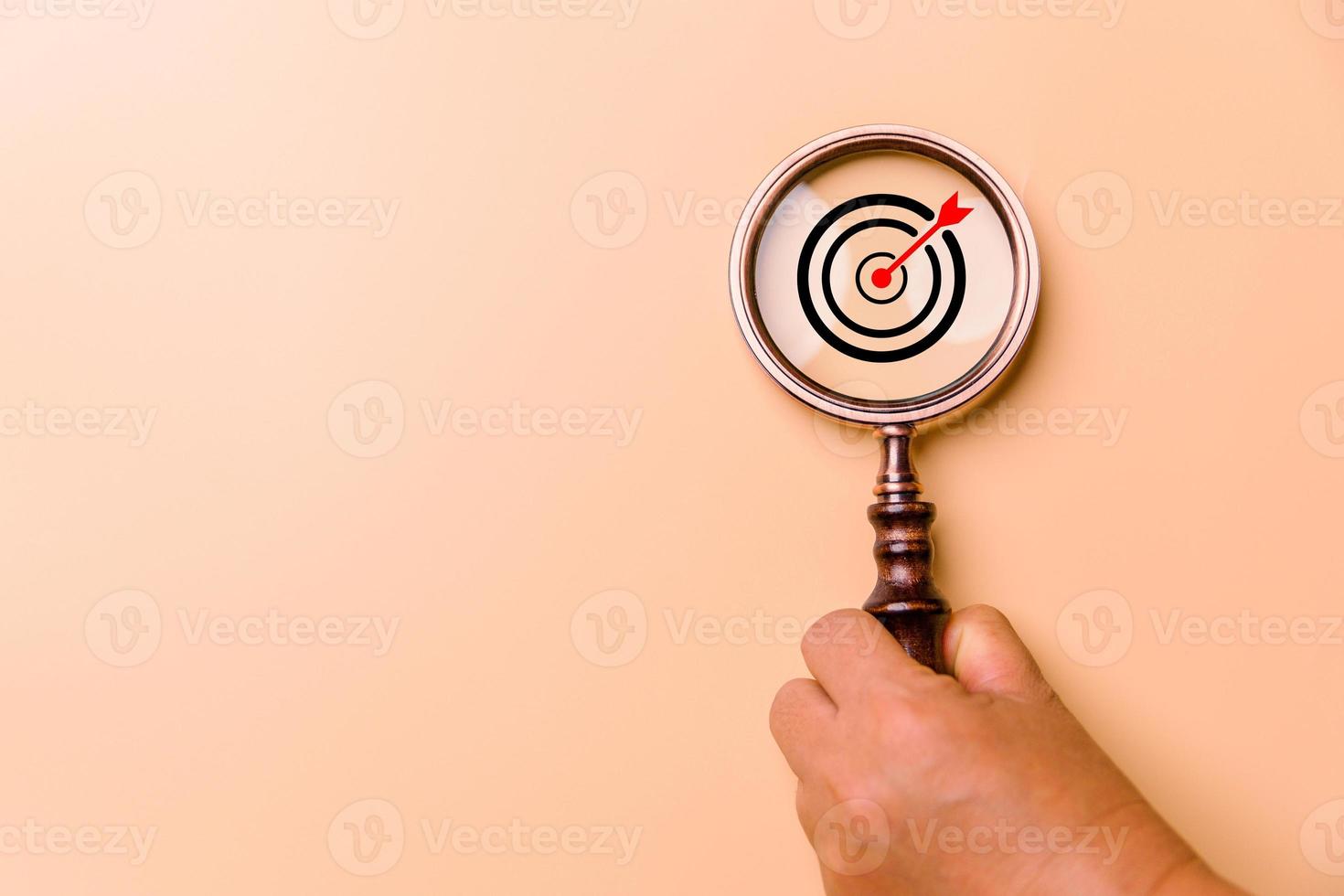 Hand holding target board inside vintage magnifying glass for focus business objective on orange background and copy space. Search, goal, strategy, success. successful marketing strategy goals photo