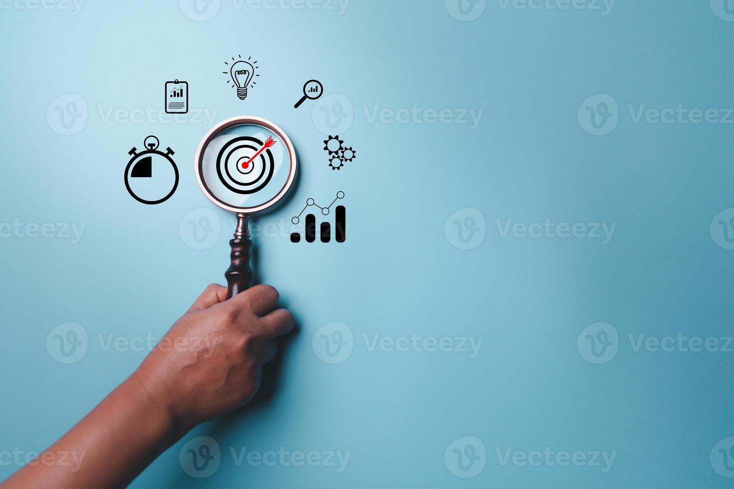 Hand holding target board inside vintage magnifying glass for focus business objective on blue background and copy space. Search, goal, strategy, success. successful marketing strategy goals photo