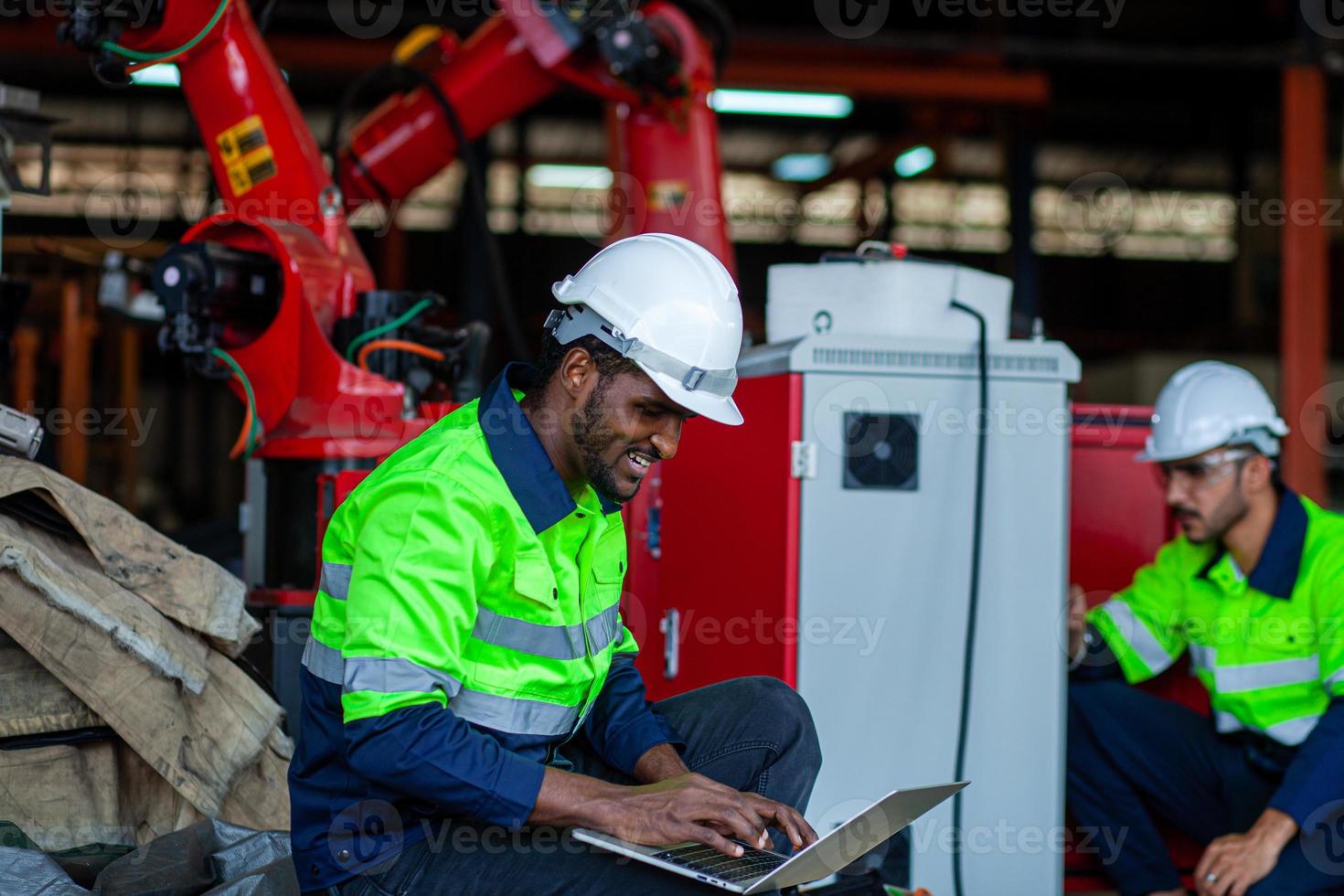 African American factory worker working with a robotic arm in a factory. Industrial robot background for automated production technology. looking at camera photo