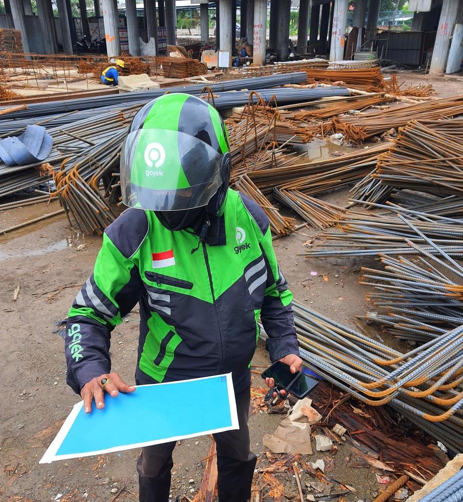 Jacarta, Indonesia en mayo 2022. un gojek conductor es cosecha arriba un paquete de documentos a ser expedido a el recipiente. foto