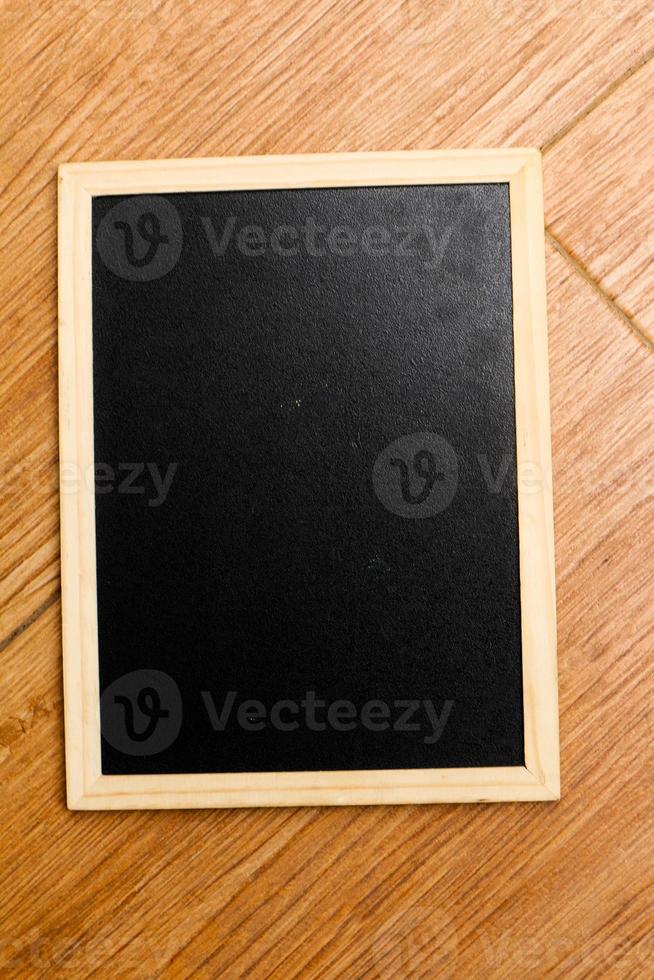 A small black chalkboard with a wooden frame rests on a wooden textured floor. photo