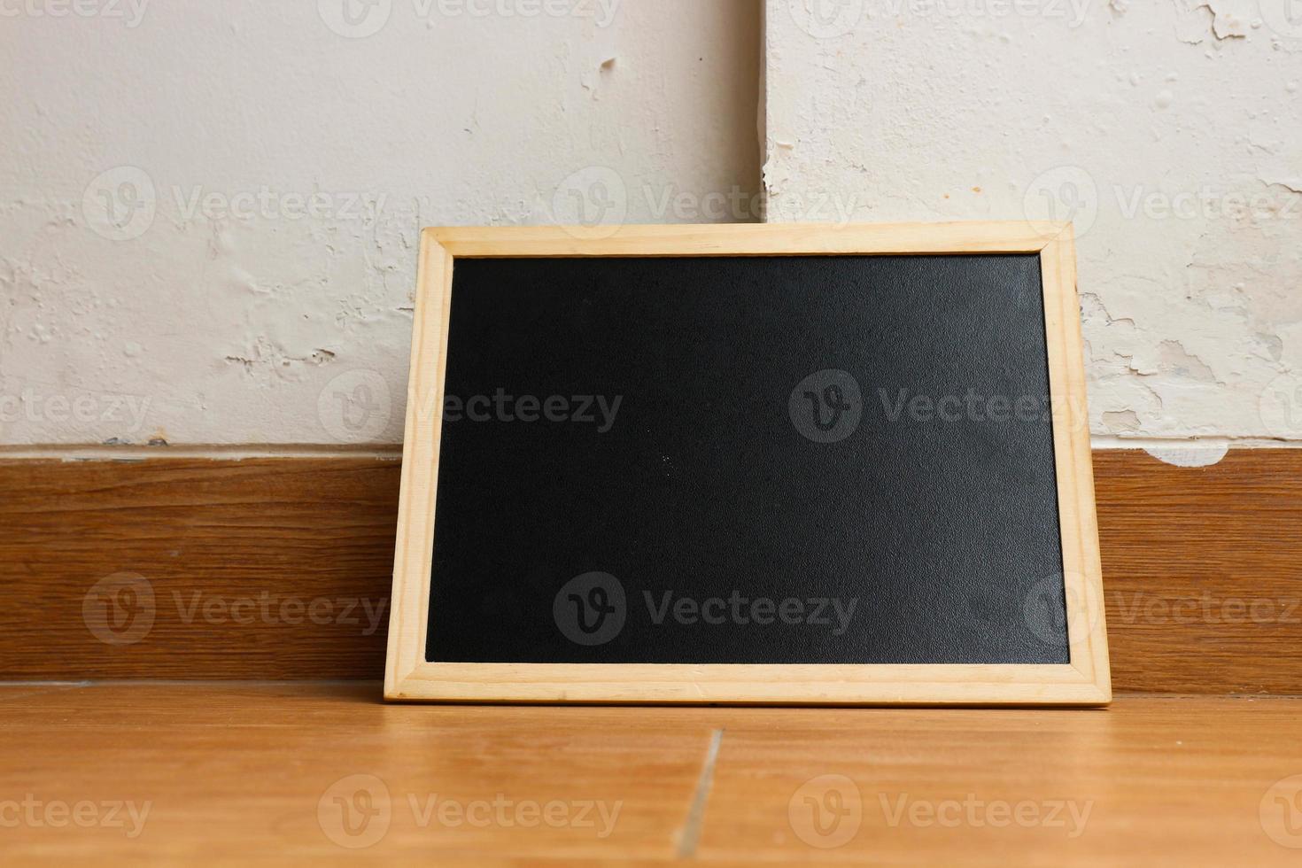 A small black chalkboard with a wooden frame rests on a wooden textured floor. photo