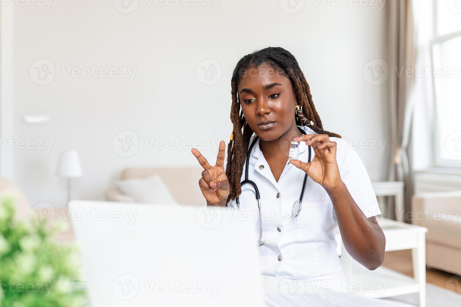 African woman doctor talking online with patient, making video call, looking at camera, young female wearing white uniform with stethoscope speaking, consulting and therapy concept photo