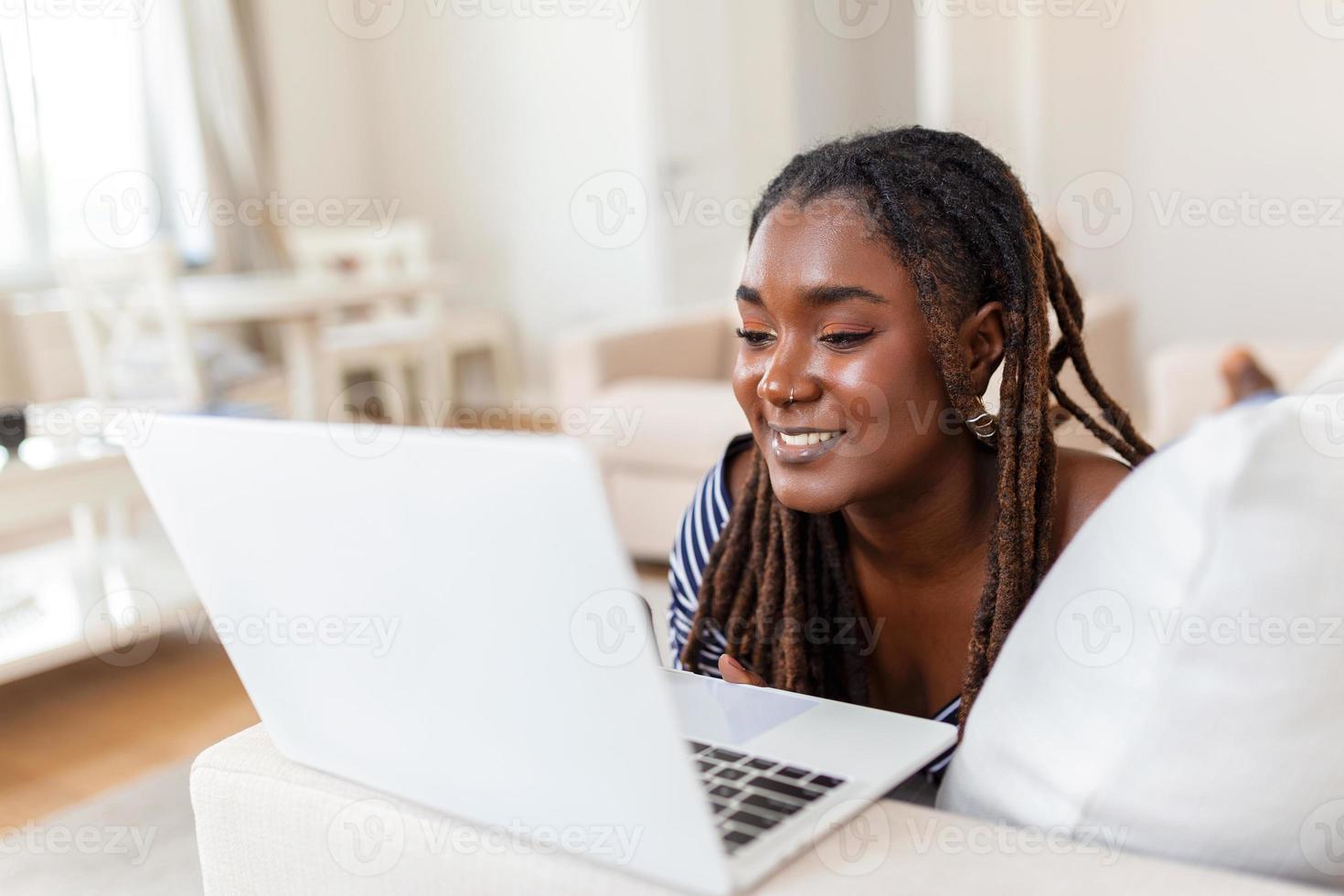 Beautiful African woman freelancer noting information for planning project doing remote job via laptop computer. Girl laughing while reading email on modern laptop device . photo