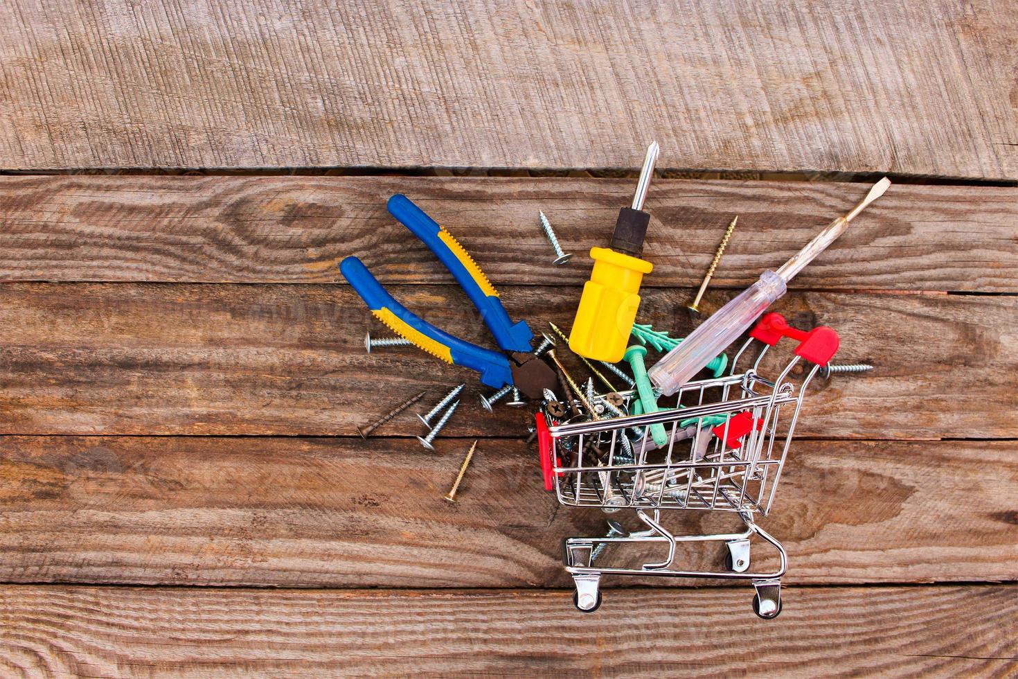 Shopping cart with construction tools on the old wood background. Toned image. photo