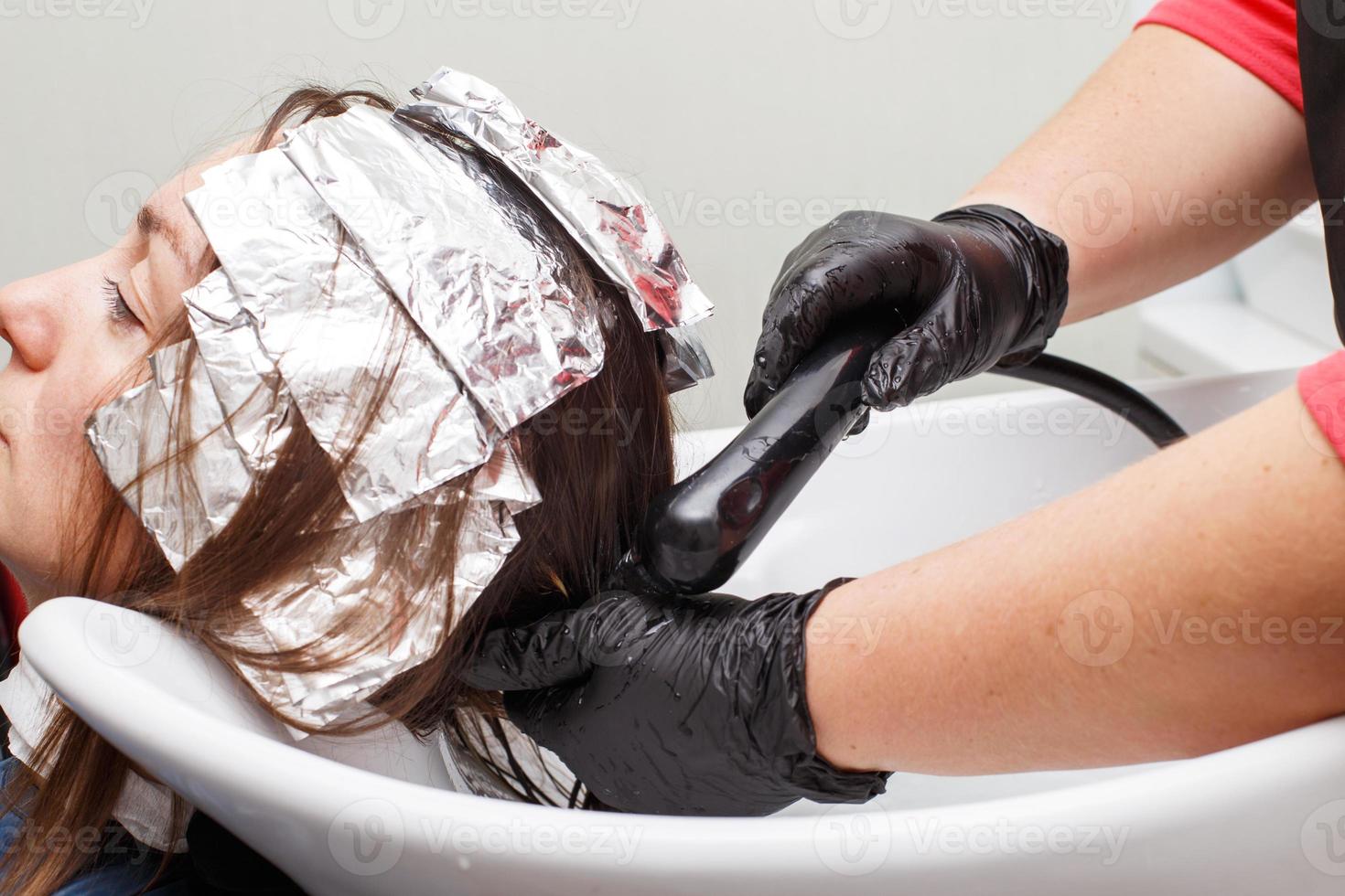 The hairdresser in black gloves paints a brunette woman's hair in the beauty salon. photo